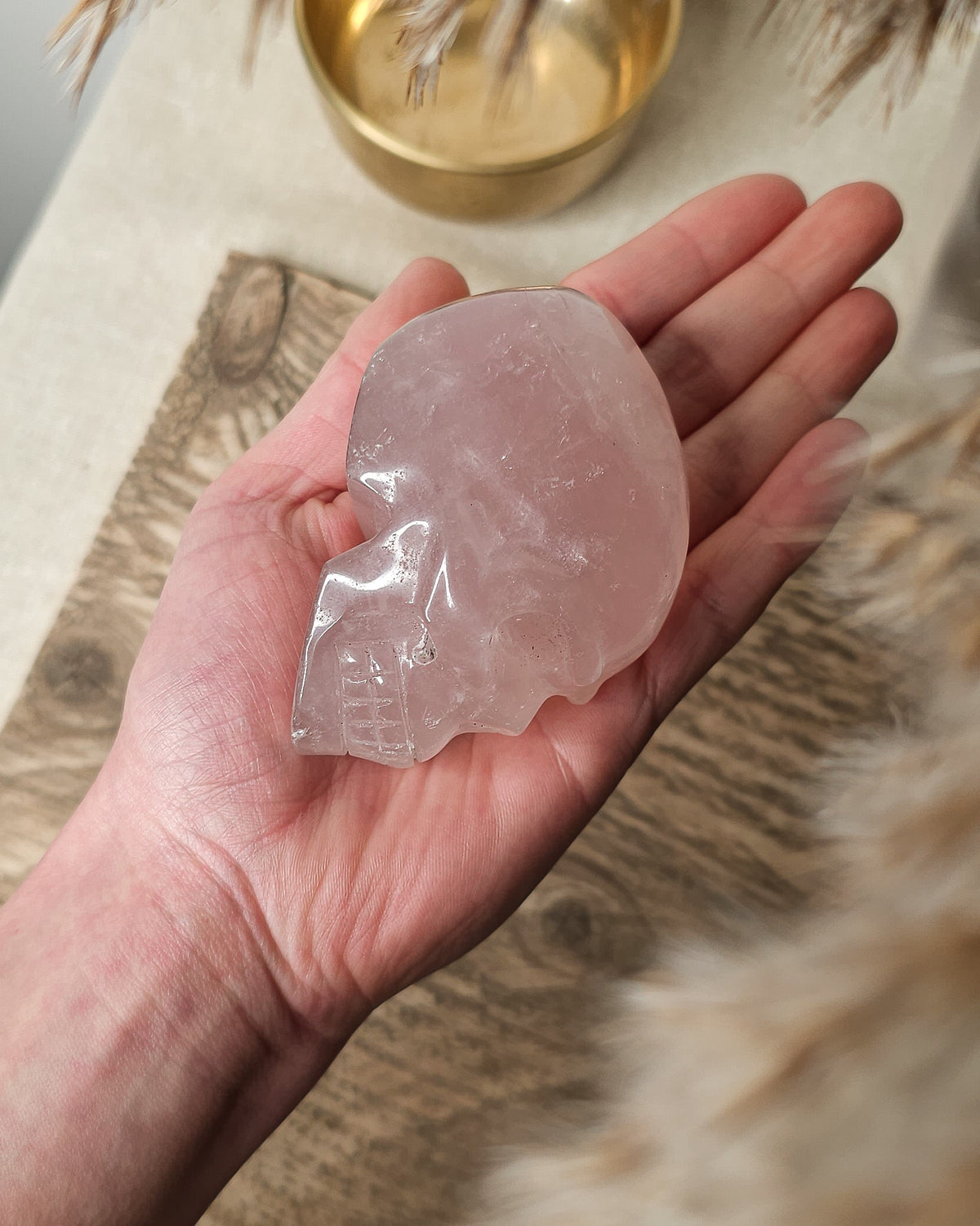Rose Quartz crystal skull carving with soft pink tones and natural cloudy patterns, polished finish, displayed as a decorative crystal piece.
