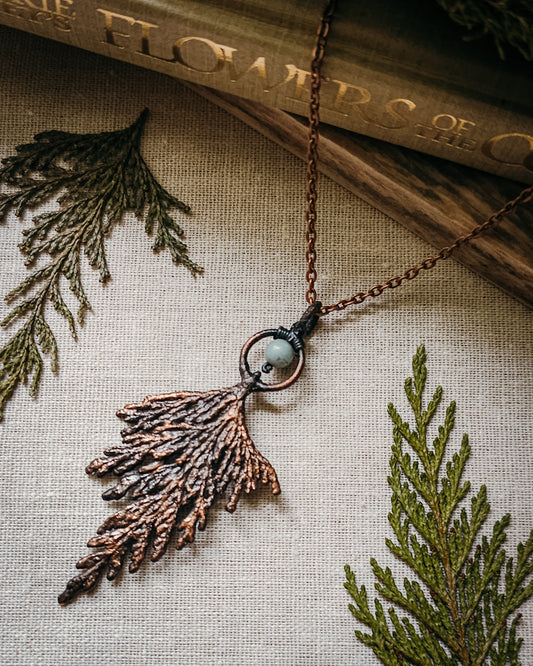 Handmade Copper electroformed Necklace with a cypress and Amazonite bead on a textured fabric background