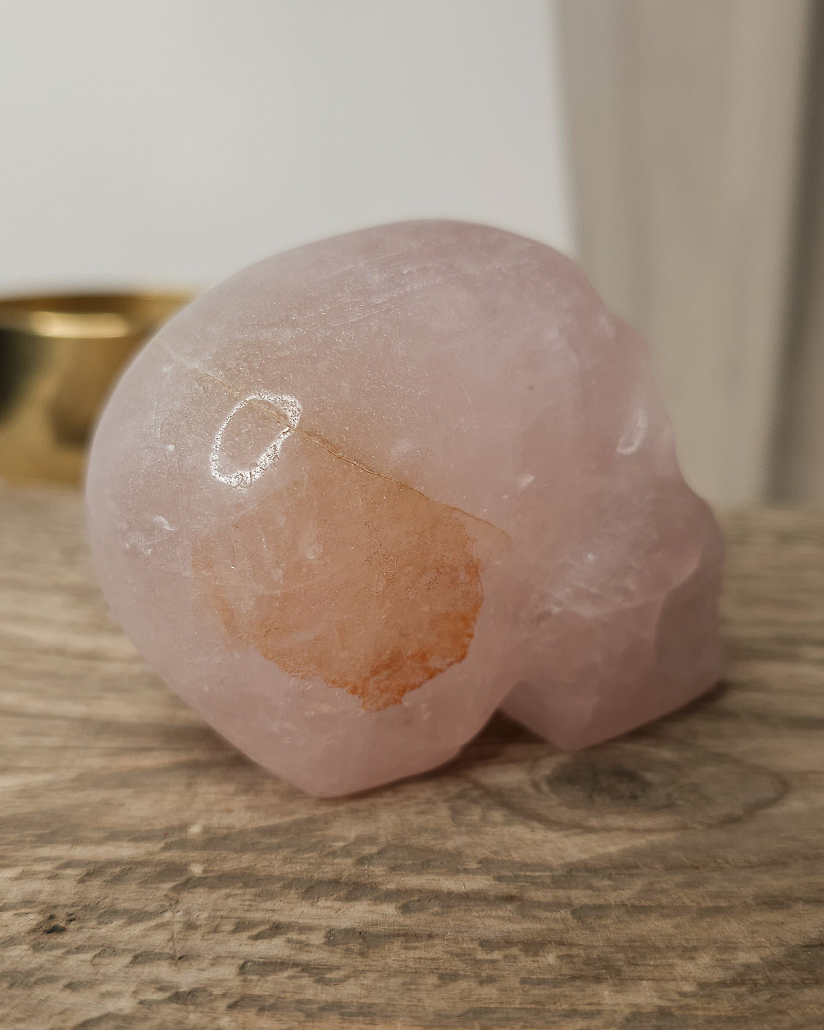Rose Quartz crystal skull with natural red Hematite inclusions, showing soft pink tones and a reddish patch at the back.