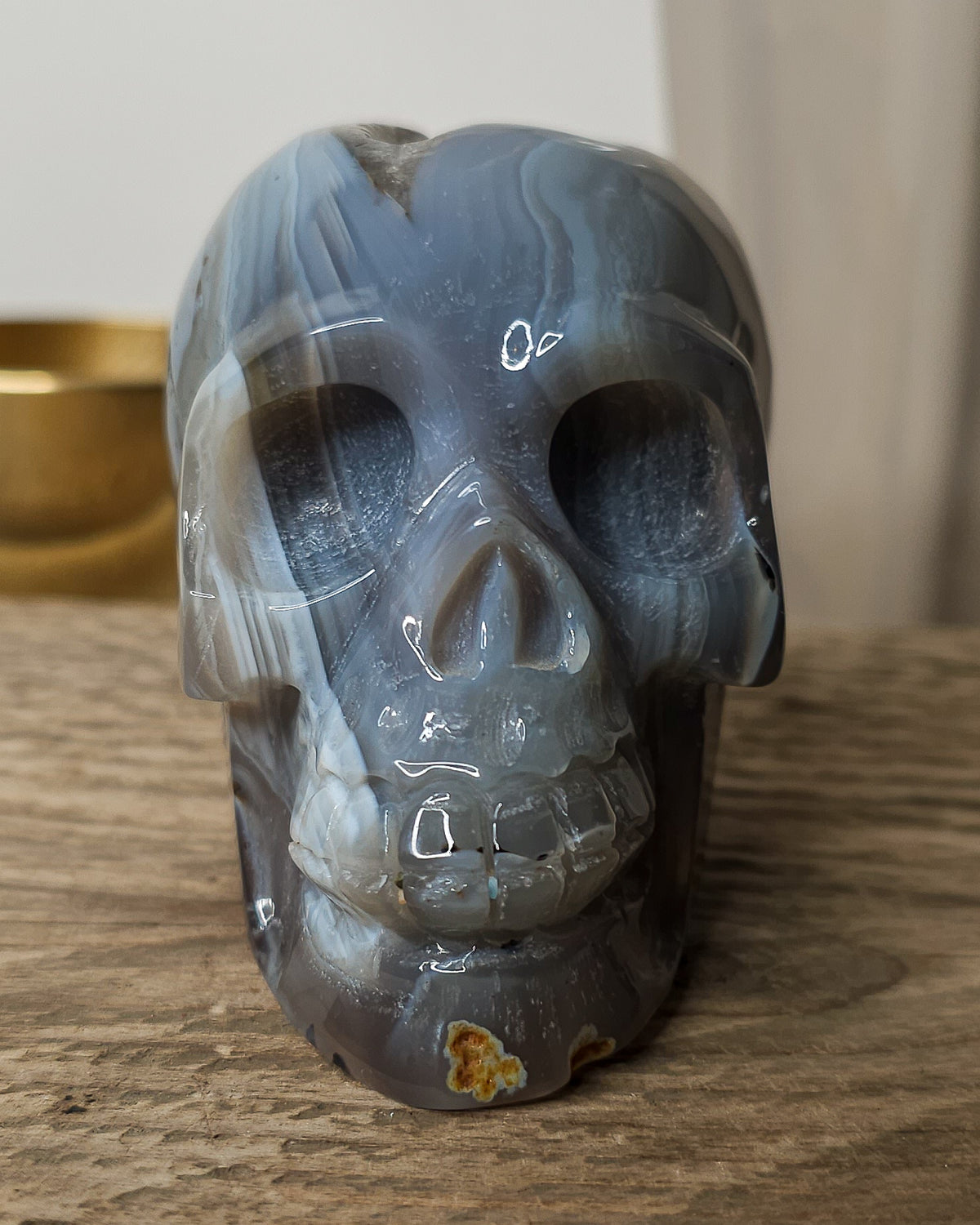 Blue Agate skull carving with layered pale blue and grey bands, a natural brown inclusion along the side and a sparkling druzy crystal cavity at the top.