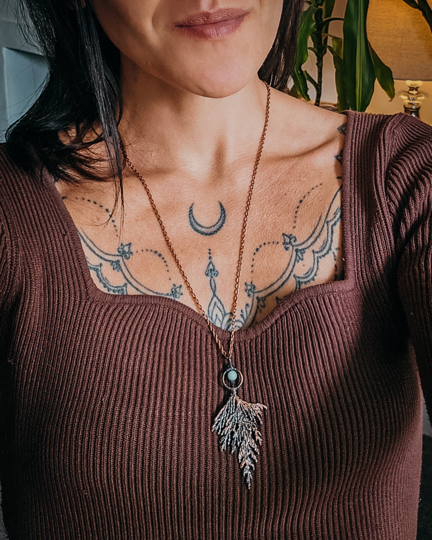 Person wearing a brown ribbed top with a Handmade Copper electroformed Necklace with a cypress and Amazonite bead, visible tattoos on chest and neck.