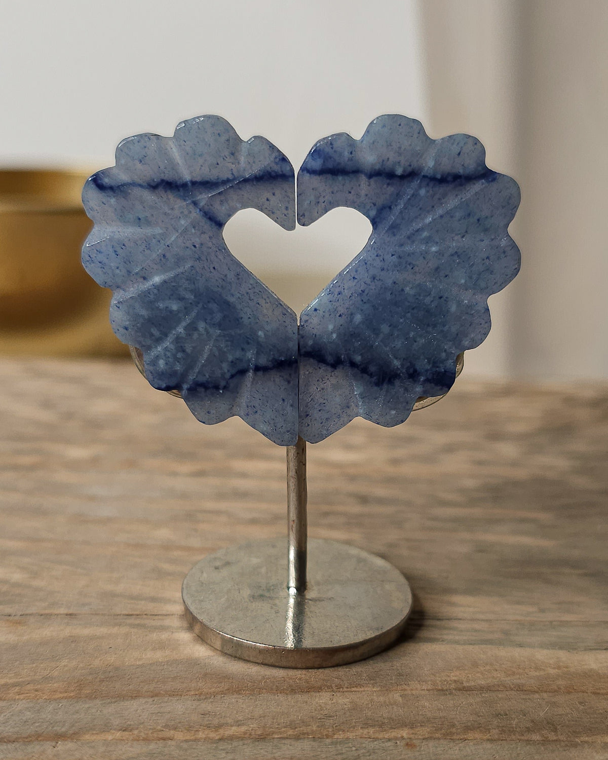 Blue Aventurine heart carving with a heart-shaped opening, featuring soft blue tones, darker natural bands and speckled patterns, displayed on a metal stand