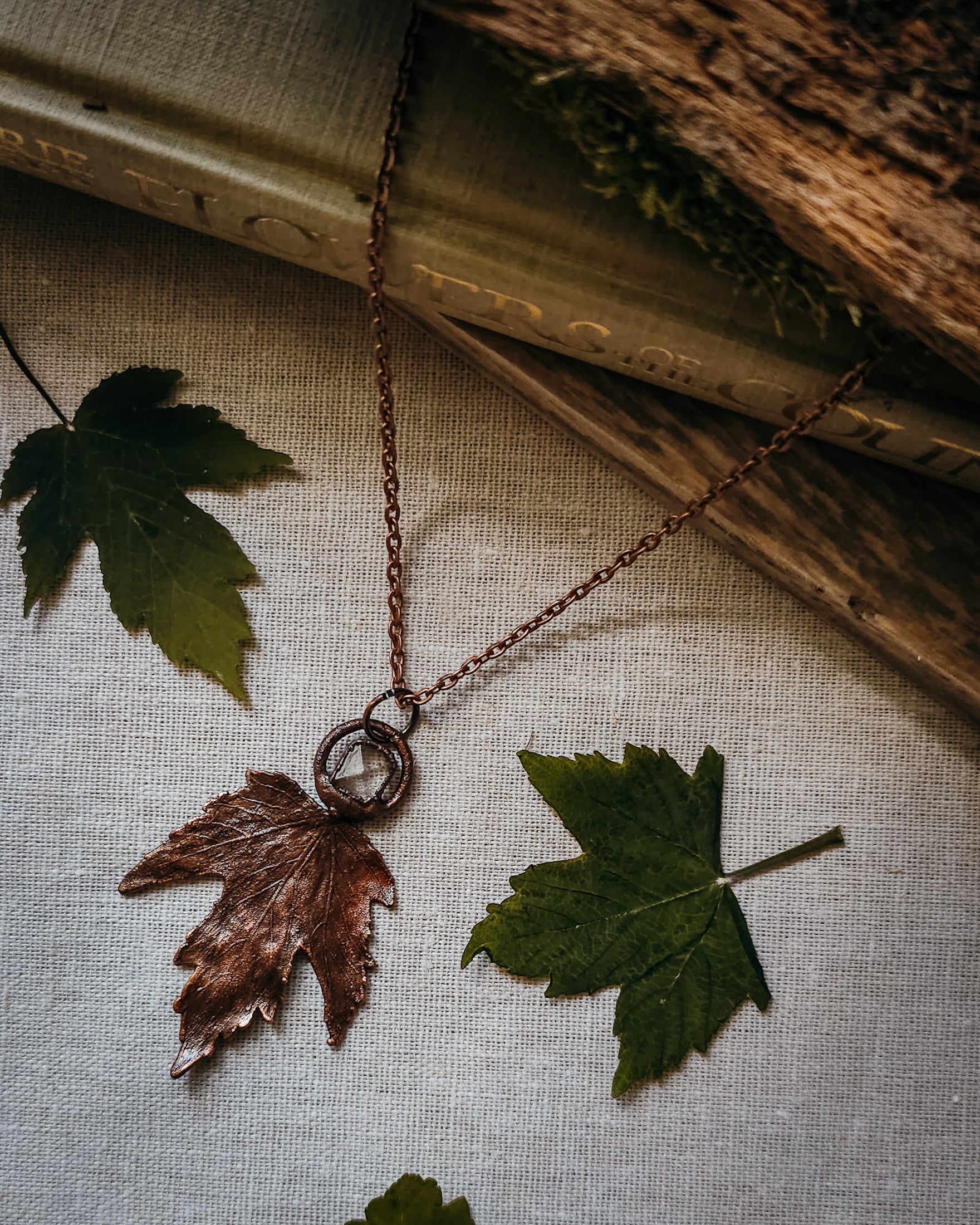 Copper electroformed Necklace with maple leaf pendant and Quartz crystal on a textured surface with leaves