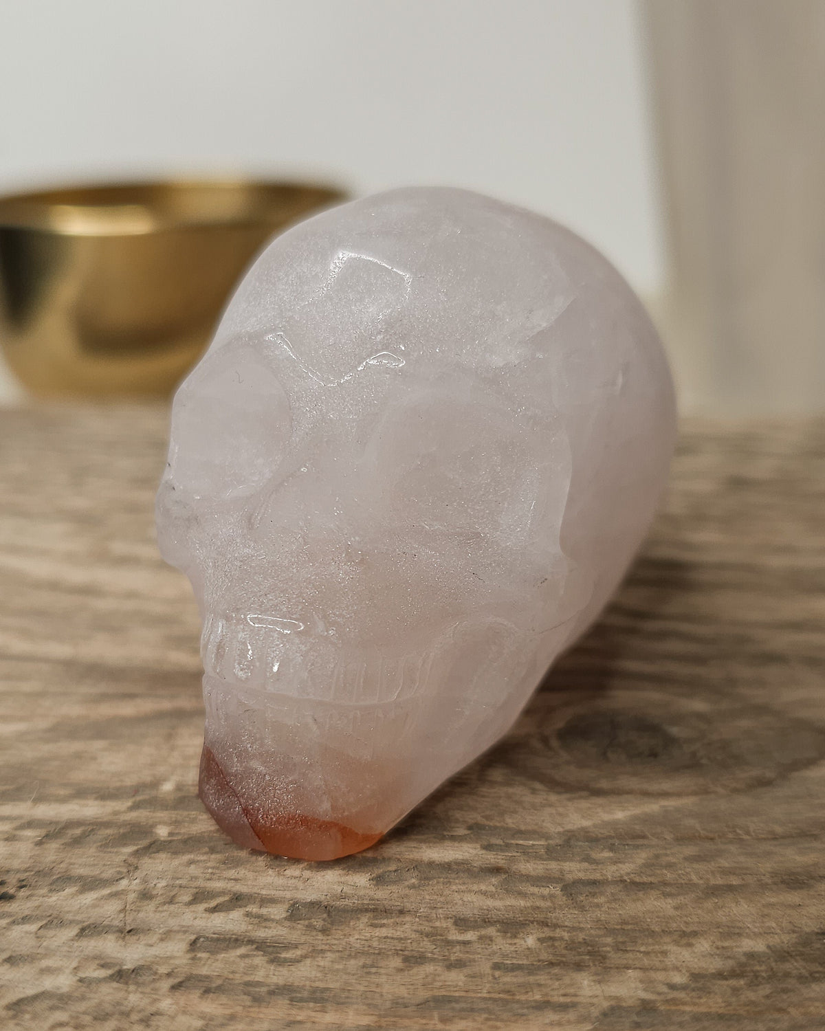Rose Quartz crystal skull with natural red Hematite inclusions, showing soft pink tones and a reddish patch at the base.