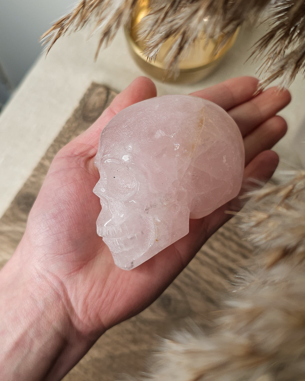 Rose Quartz crystal skull with natural red Hematite inclusions, showing soft pink tones and a reddish patch at the back.