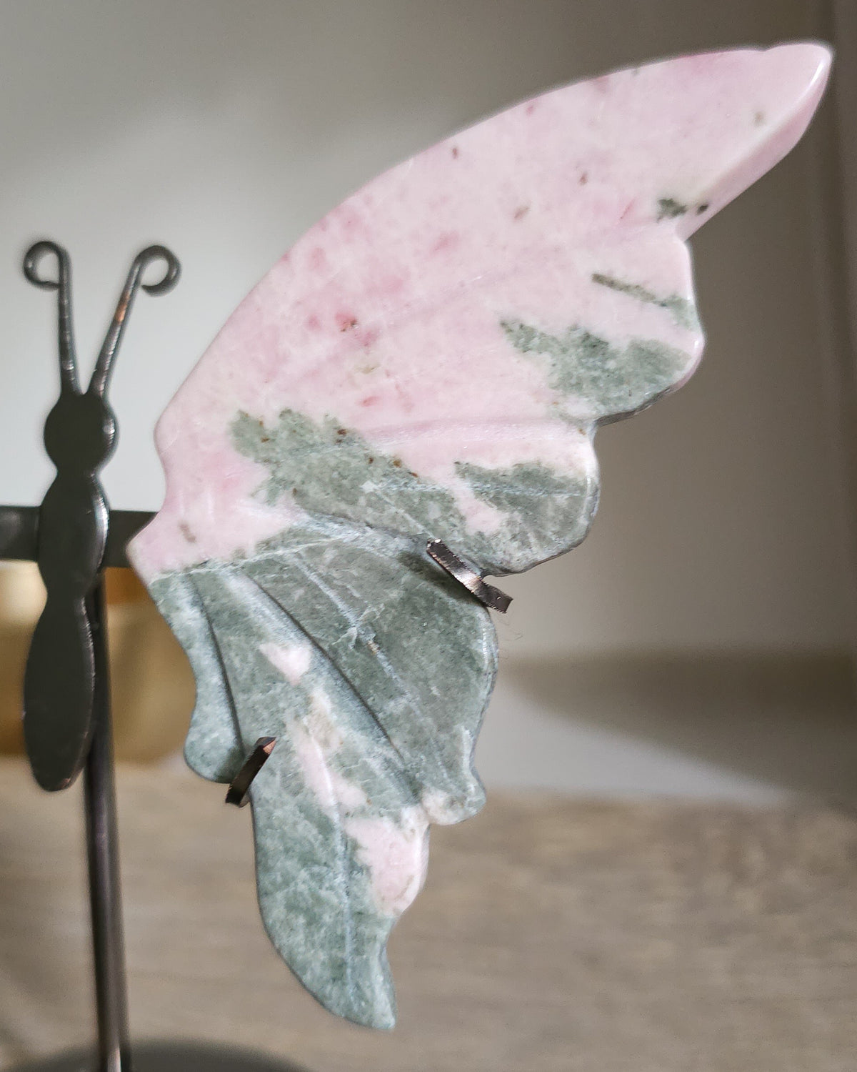 Pink Opal butterfly wings carved from natural pink opal, displayed on a black metal stand, showing soft pink and creamy tones.