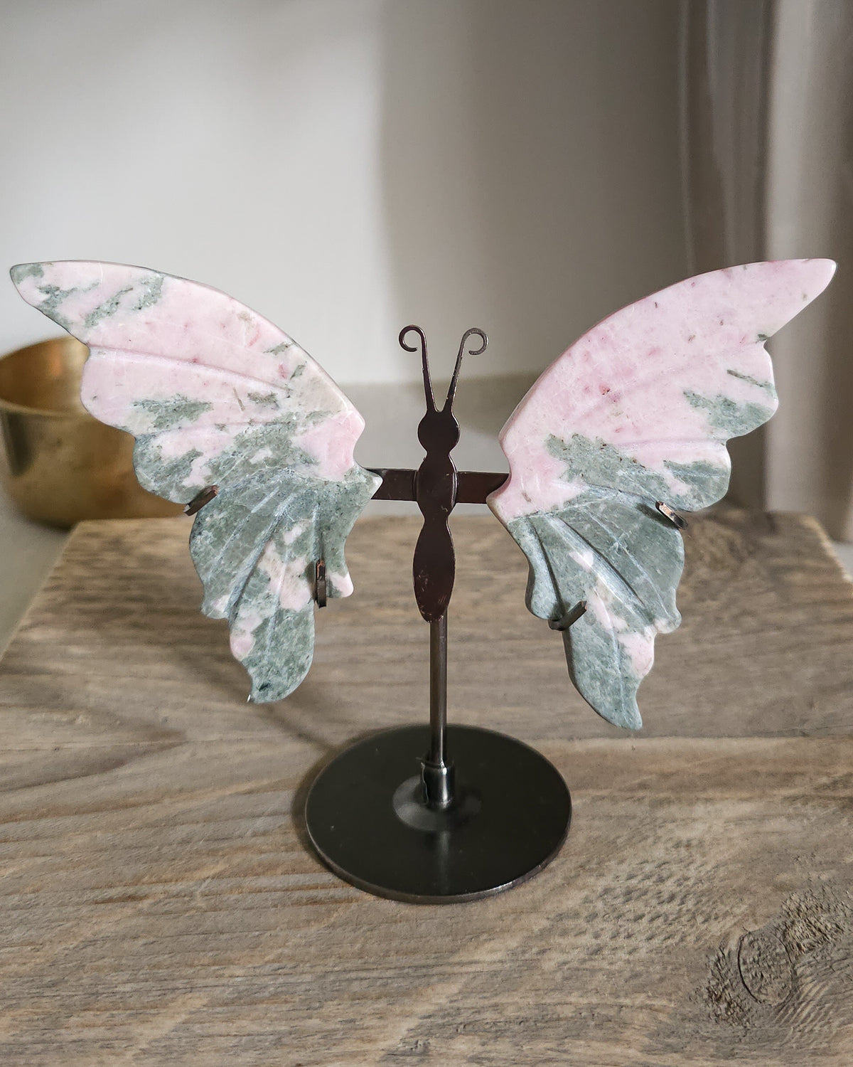 Pink Opal butterfly wings carved from natural pink opal, displayed on a black metal stand, showing soft pink and creamy tones.