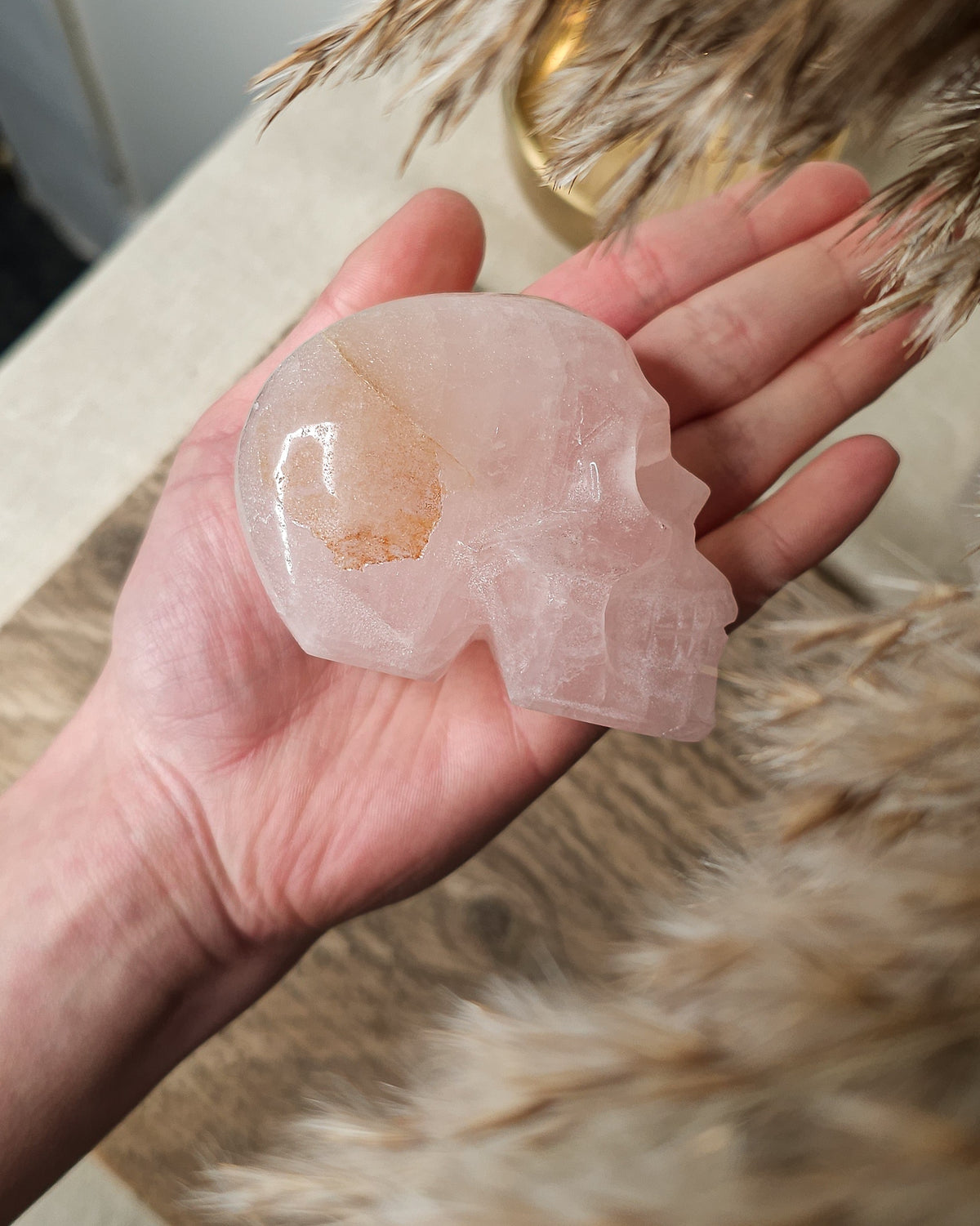 Rose Quartz crystal skull with natural red Hematite inclusions, showing soft pink tones and a reddish patch at the back.