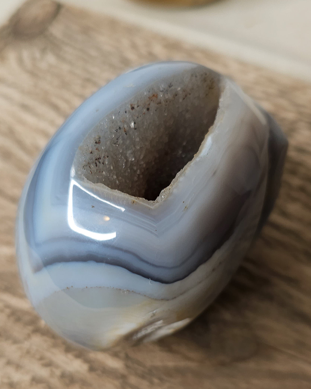 Blue Agate skull carving with layered pale blue and grey bands, a natural brown inclusion along the side and a sparkling druzy crystal cavity at the top.