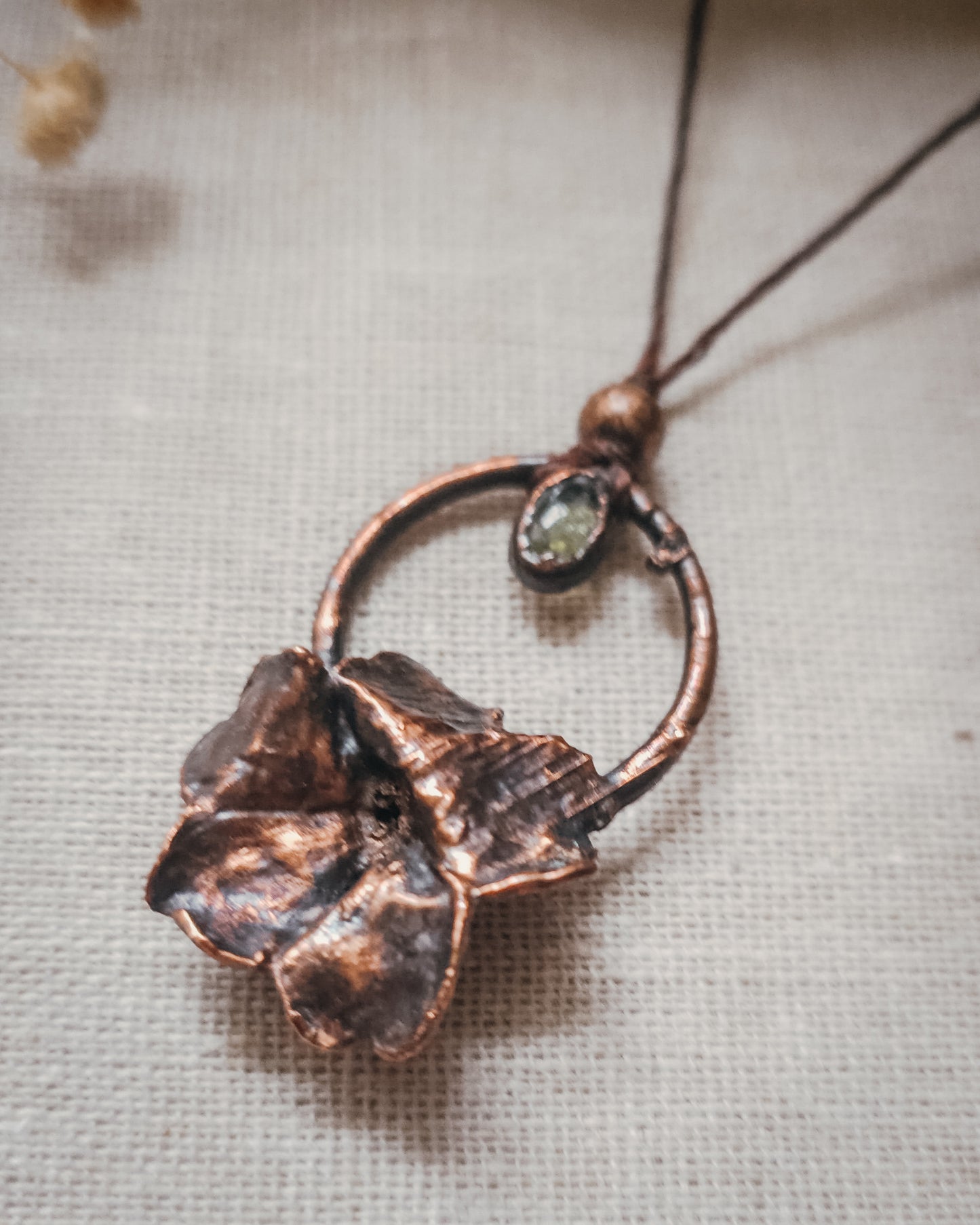 Handcrafted copper electroformed Primrose flower necklace featuring a natural Green Tourmaline stone, green and pink Tourmaline beads, brass accent beads on an adjustable cord. Created from a real Primrose flower gathered in Scotland and inspired by woodland folklore, renewal, and the magic of hidden pathways.