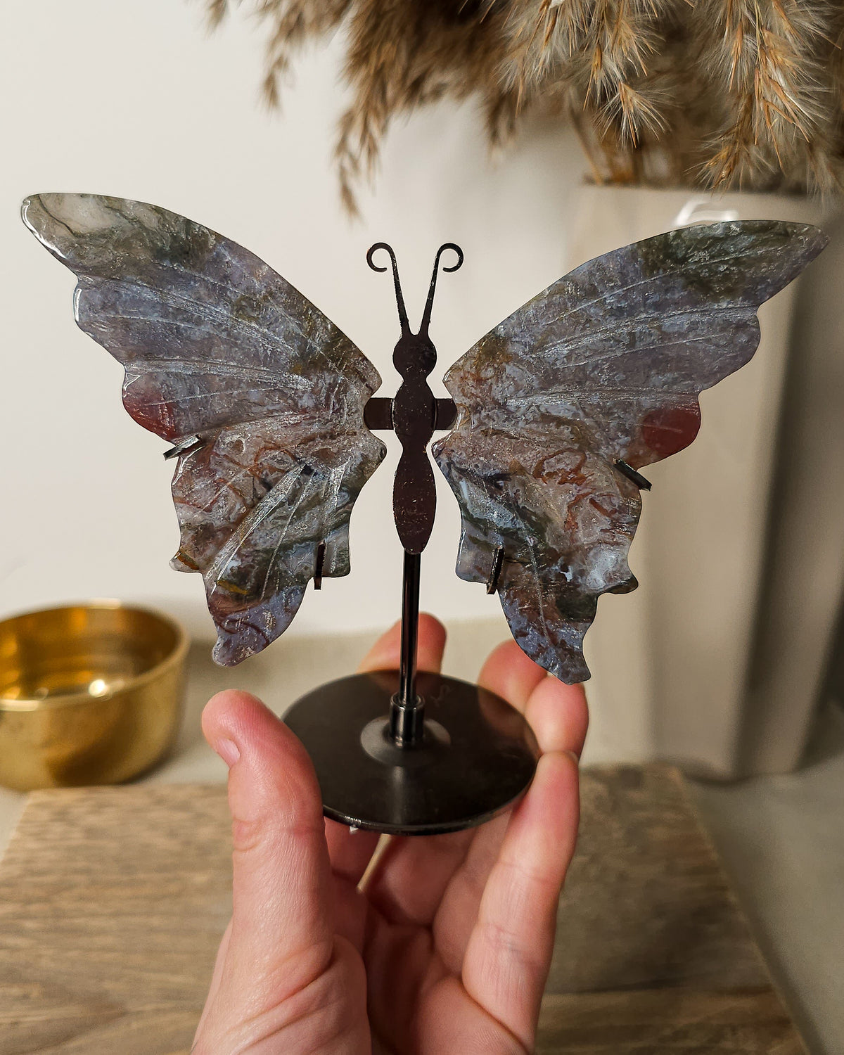 Moss Agate butterfly wings on a black metal stand, featuring natural grey, green, brown and reddish patterns.
