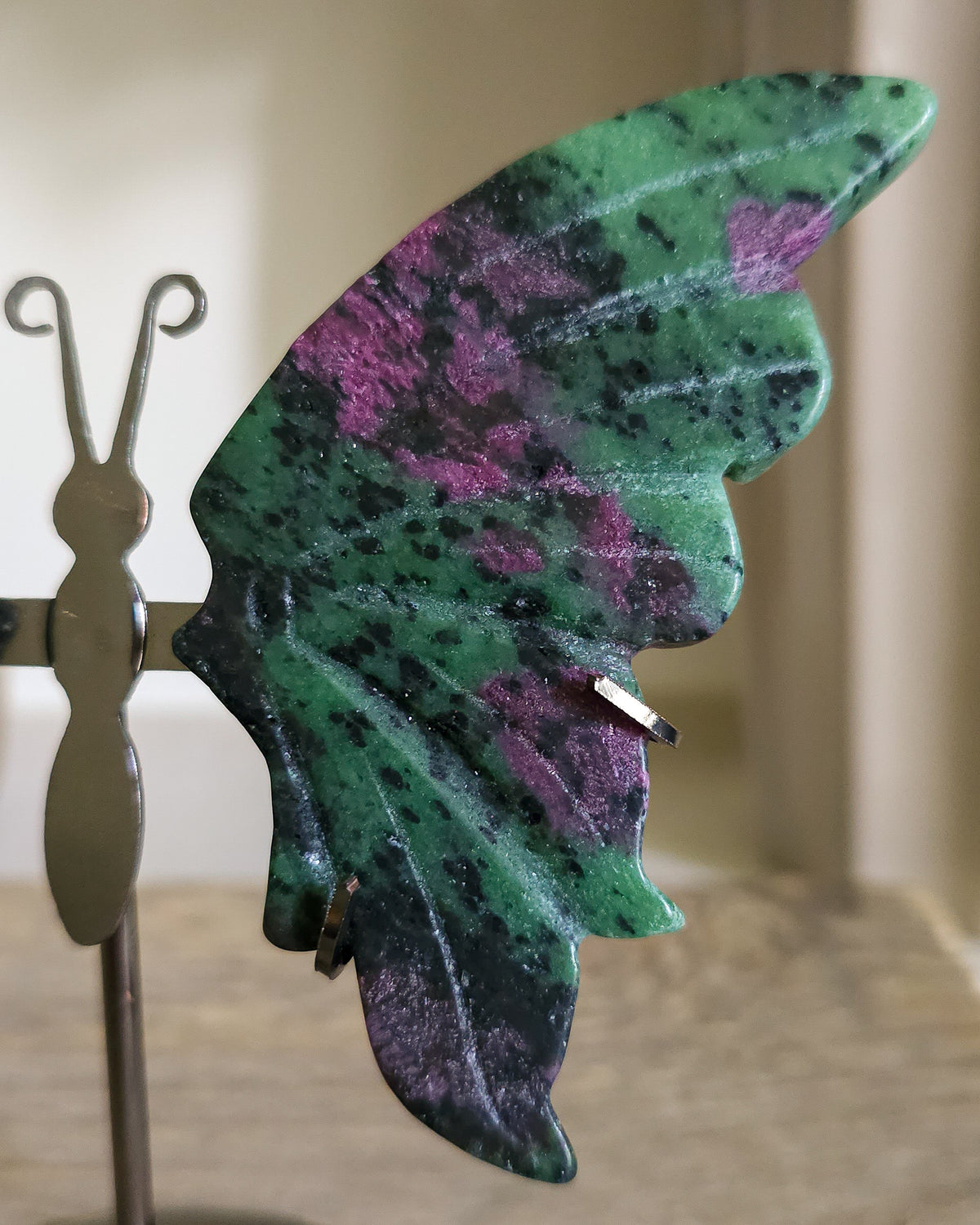Ruby in Zoisite butterfly wings with fluorescent Ruby inclusions on a black metal stand, glowing vivid pink-red under UV light.. 