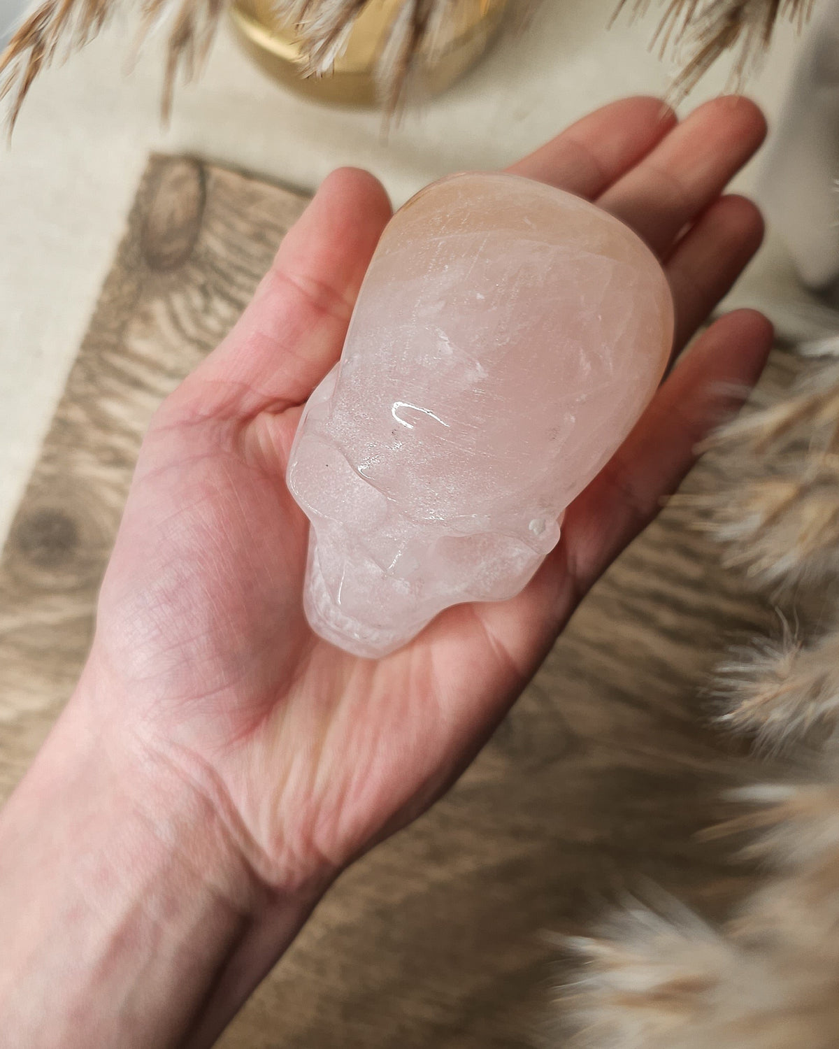 Rose Quartz crystal skull with natural red Hematite inclusions, showing soft pink tones and a reddish patch at the back.