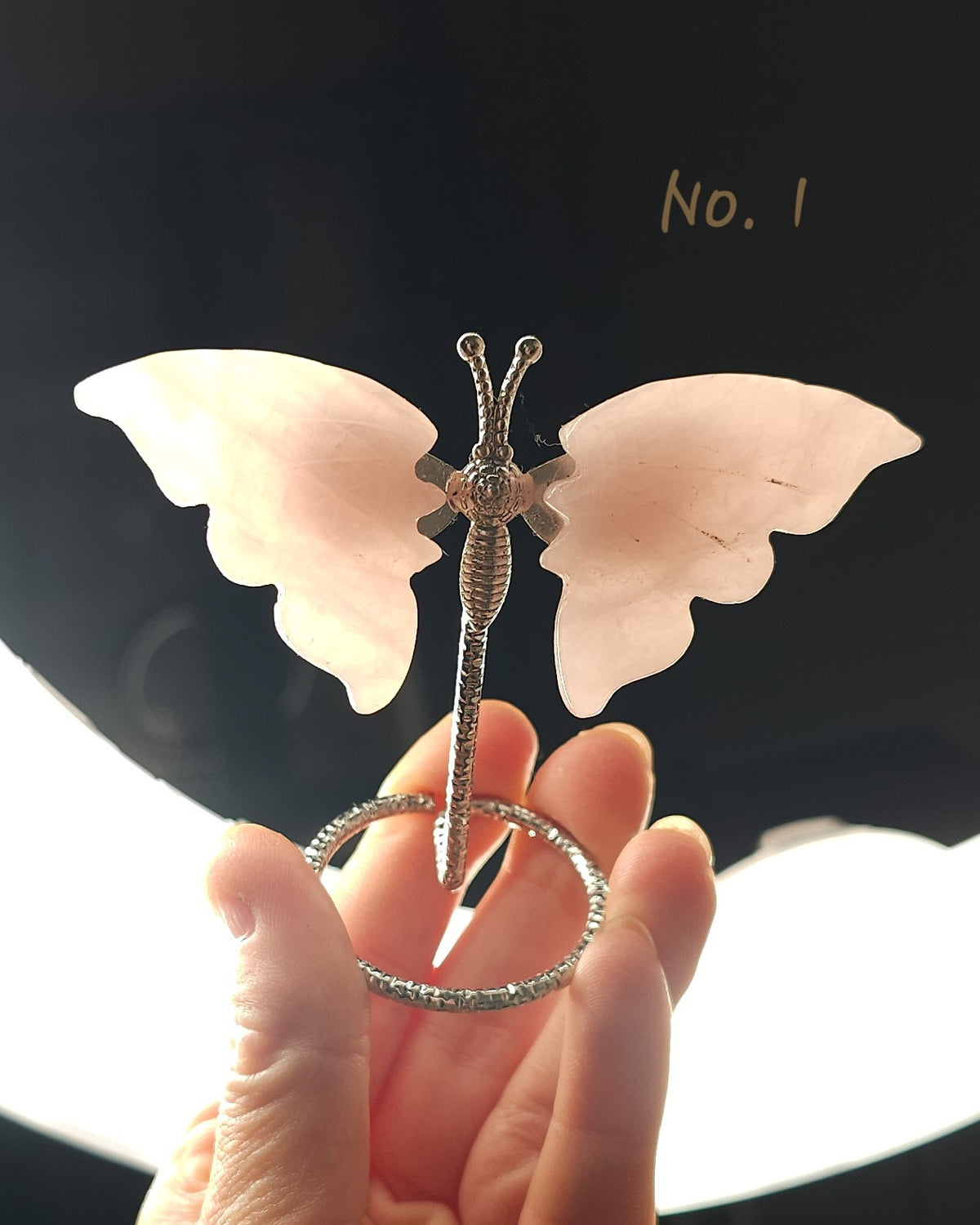 Polished rose quartz crystal butterfly carving with soft pink wings on a silver-tone display stand
