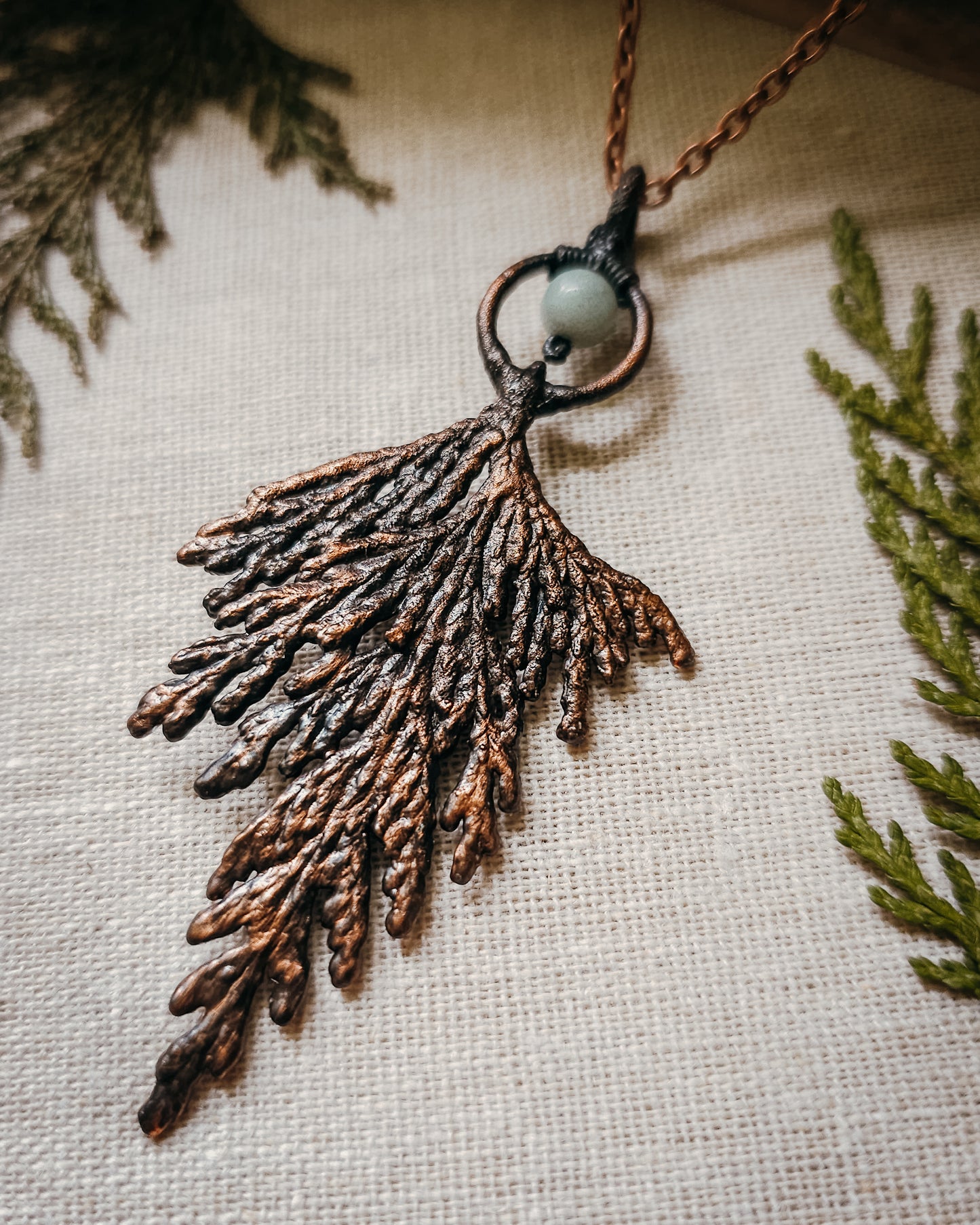 Handmade Copper electroformed Necklace with a cypress and Amazonite bead on a textured fabric background