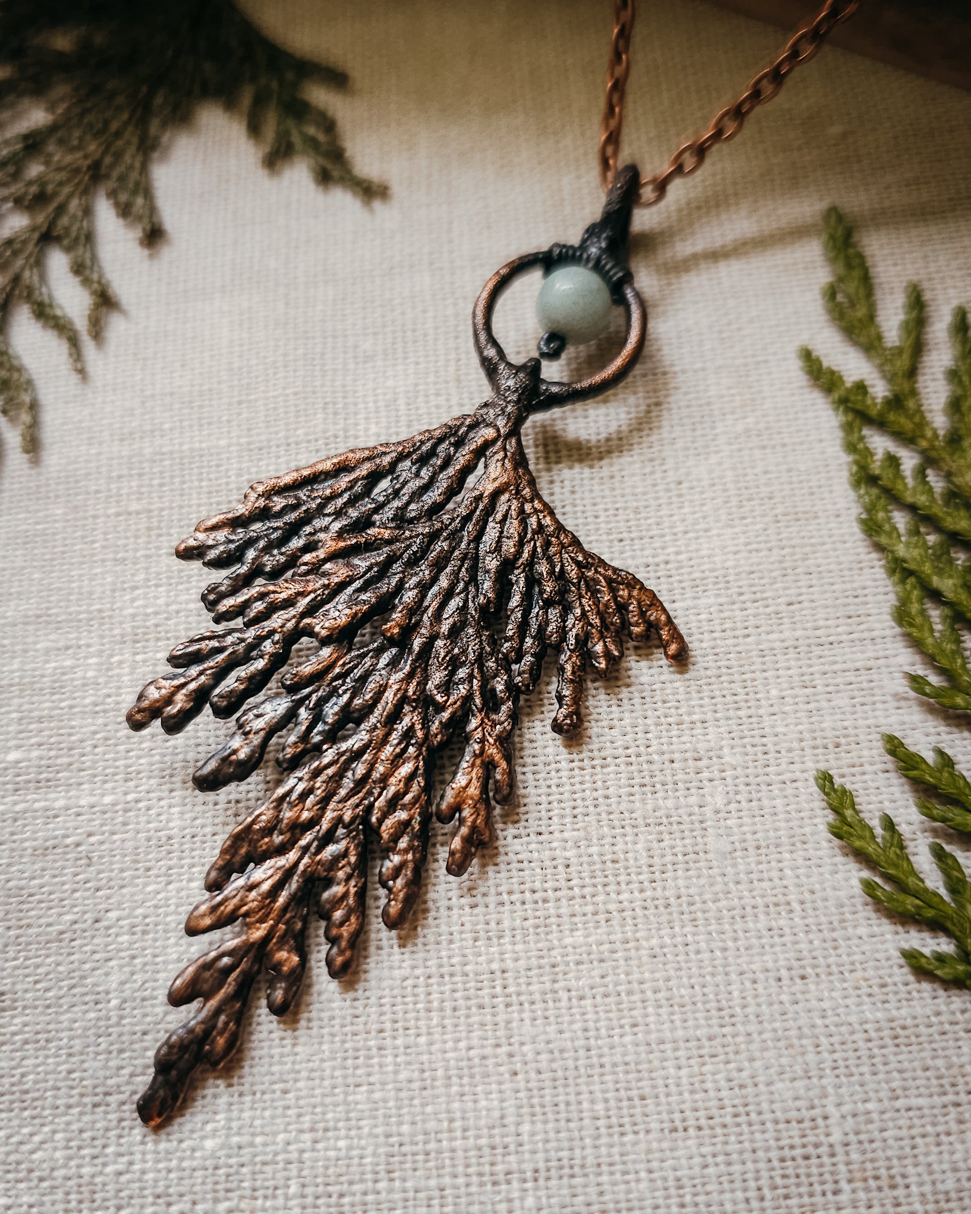 Handmade Copper electroformed Necklace with a cypress and Amazonite bead on a textured fabric background