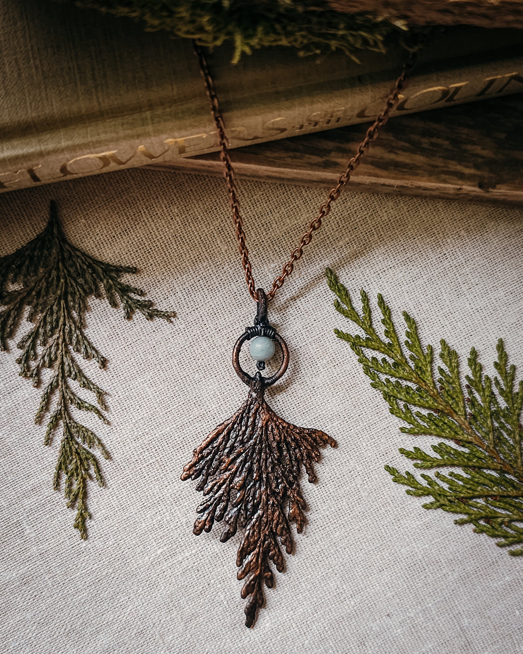 Handmade Copper electroformed Necklace with a cypress and Amazonite bead on a textured fabric background