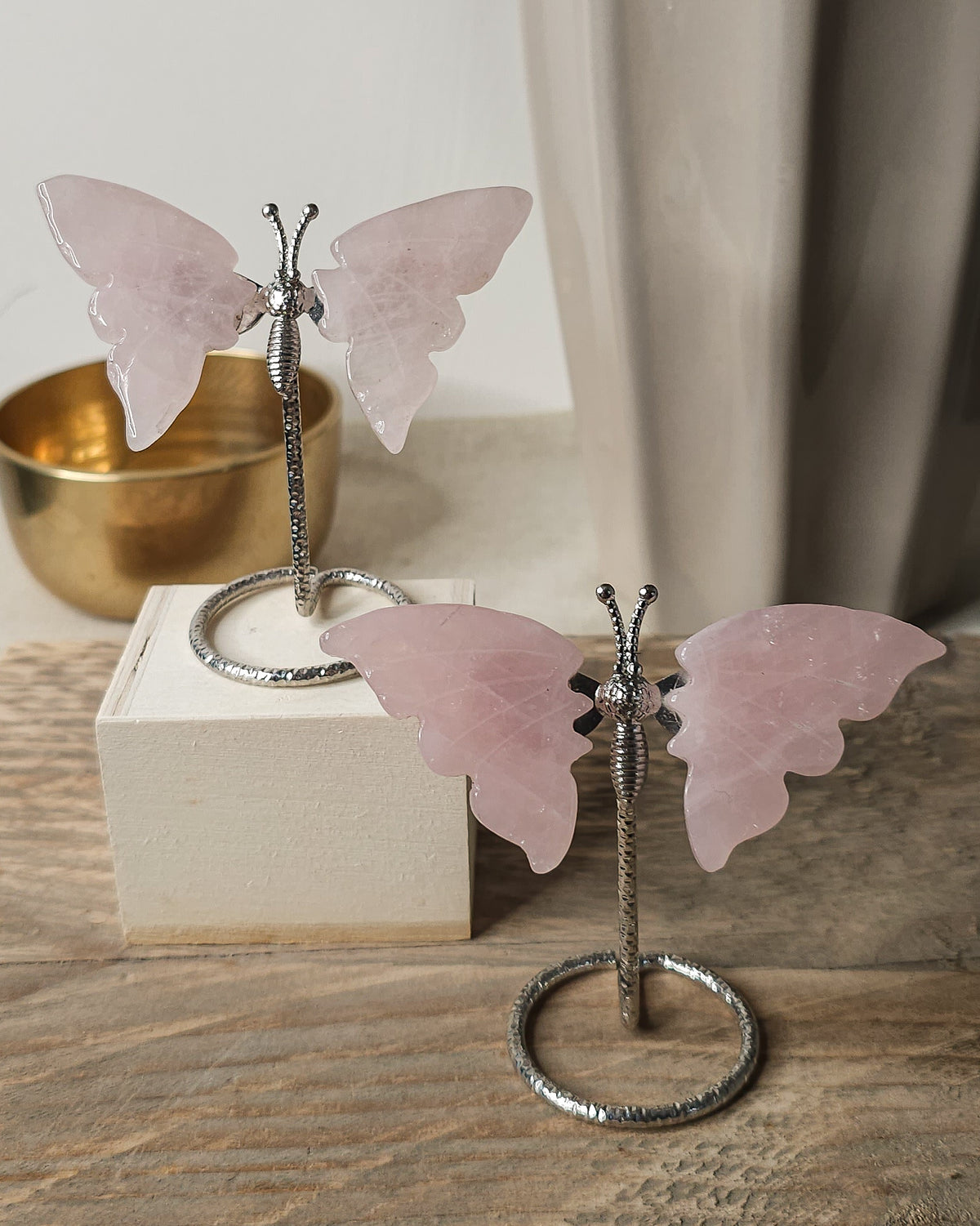 Polished rose quartz crystal butterfly carving with soft pink wings on a silver-tone display stand
