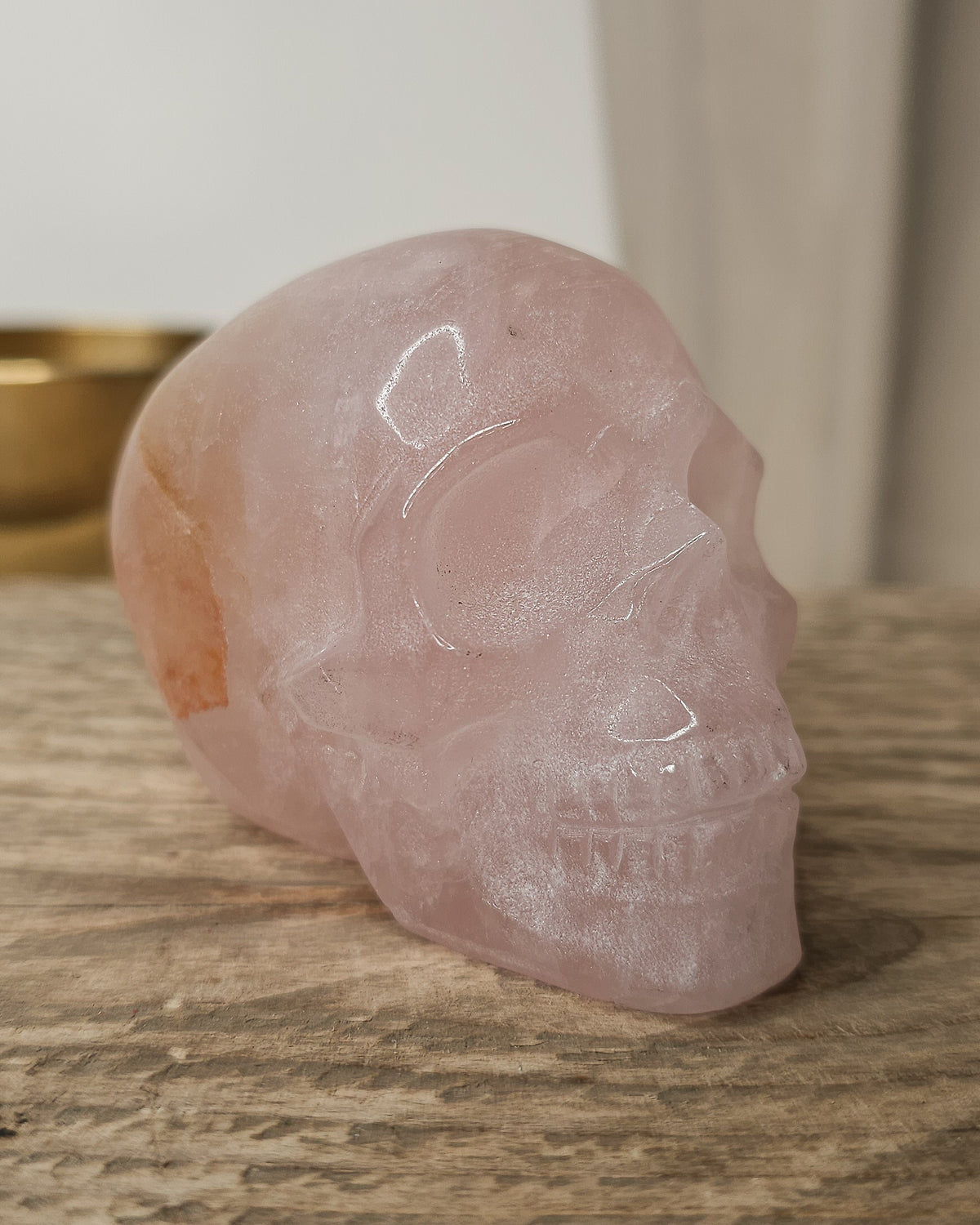 Rose Quartz crystal skull with natural red Hematite inclusions, showing soft pink tones and a reddish patch at the back.