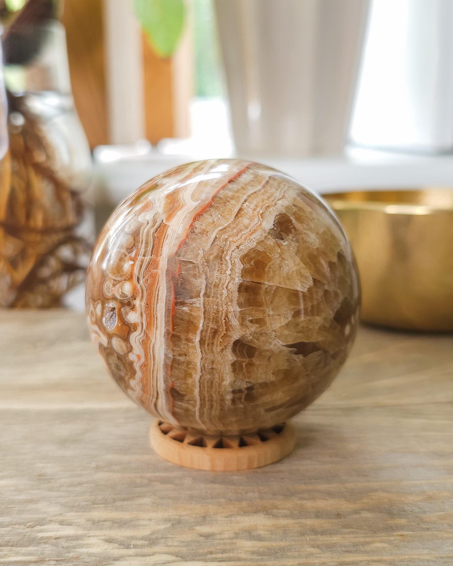 Chocolate Calcite sphere with natural druzy crystal cavities, orbicular banding and warm caramel, cream and brown patterns, displayed on a wooden stand.