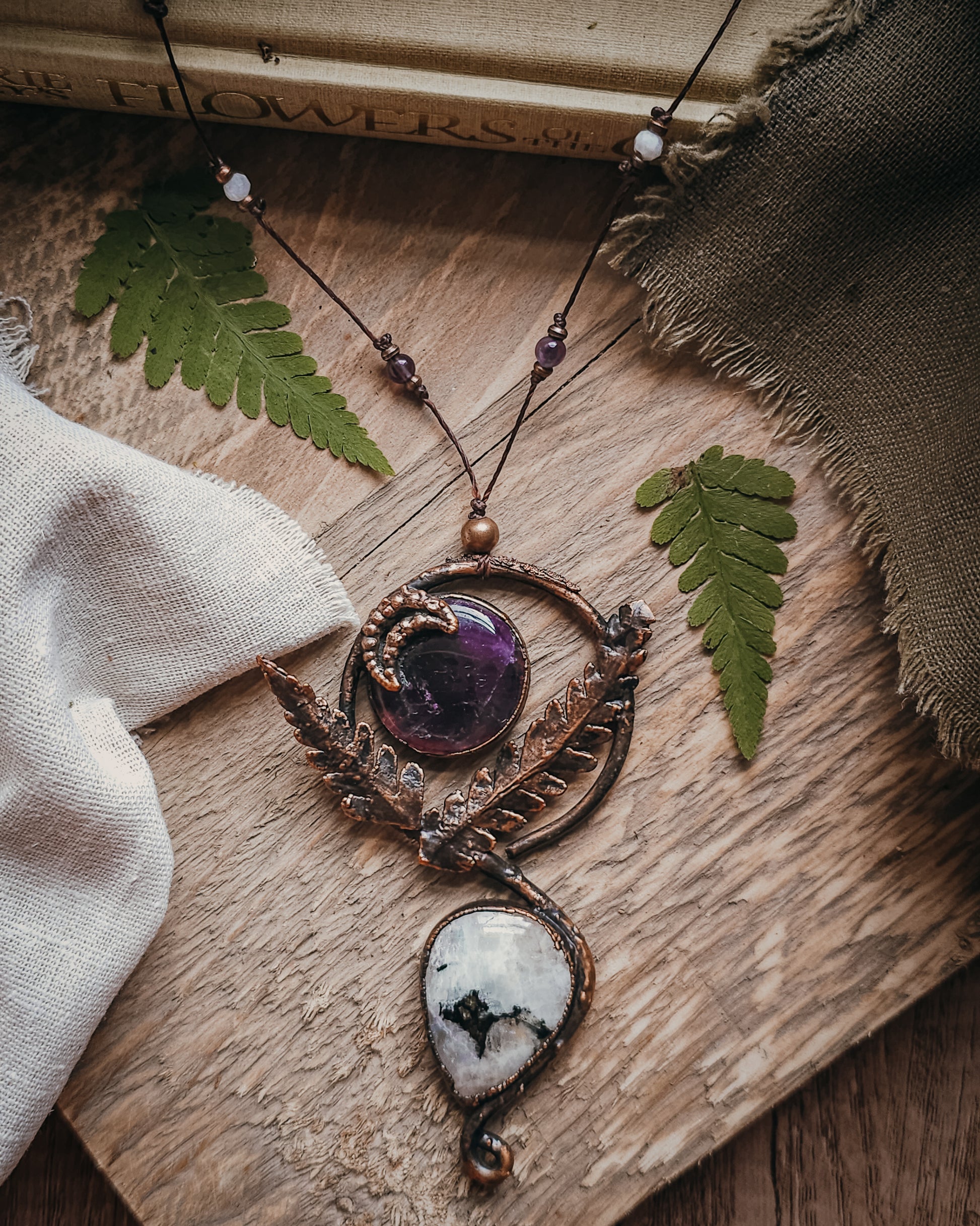 Copper electroformed Ornate pendant with amehtyst, Moonstone and fern leaves on a wooden surface with leaves